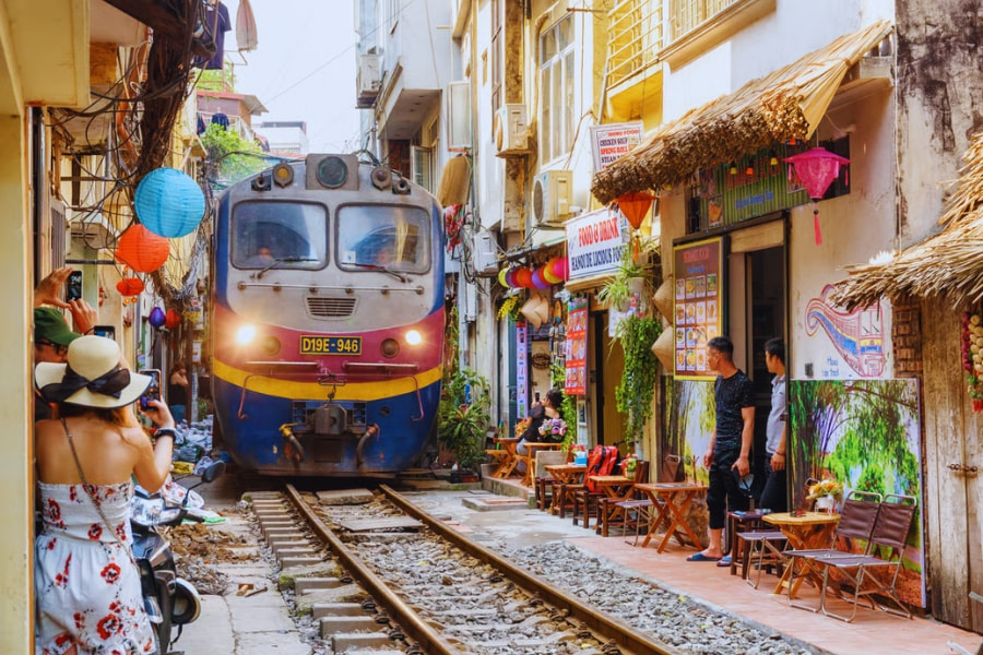 Train passing through narrow Hanoi Train Street with cafés and tourists nearby